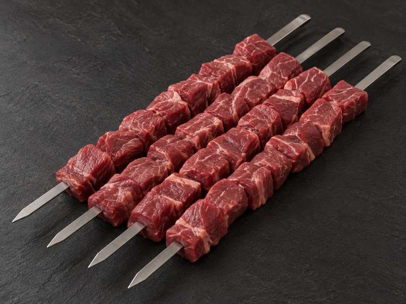 Raw lamb cubes threaded on four steel shish skewers
